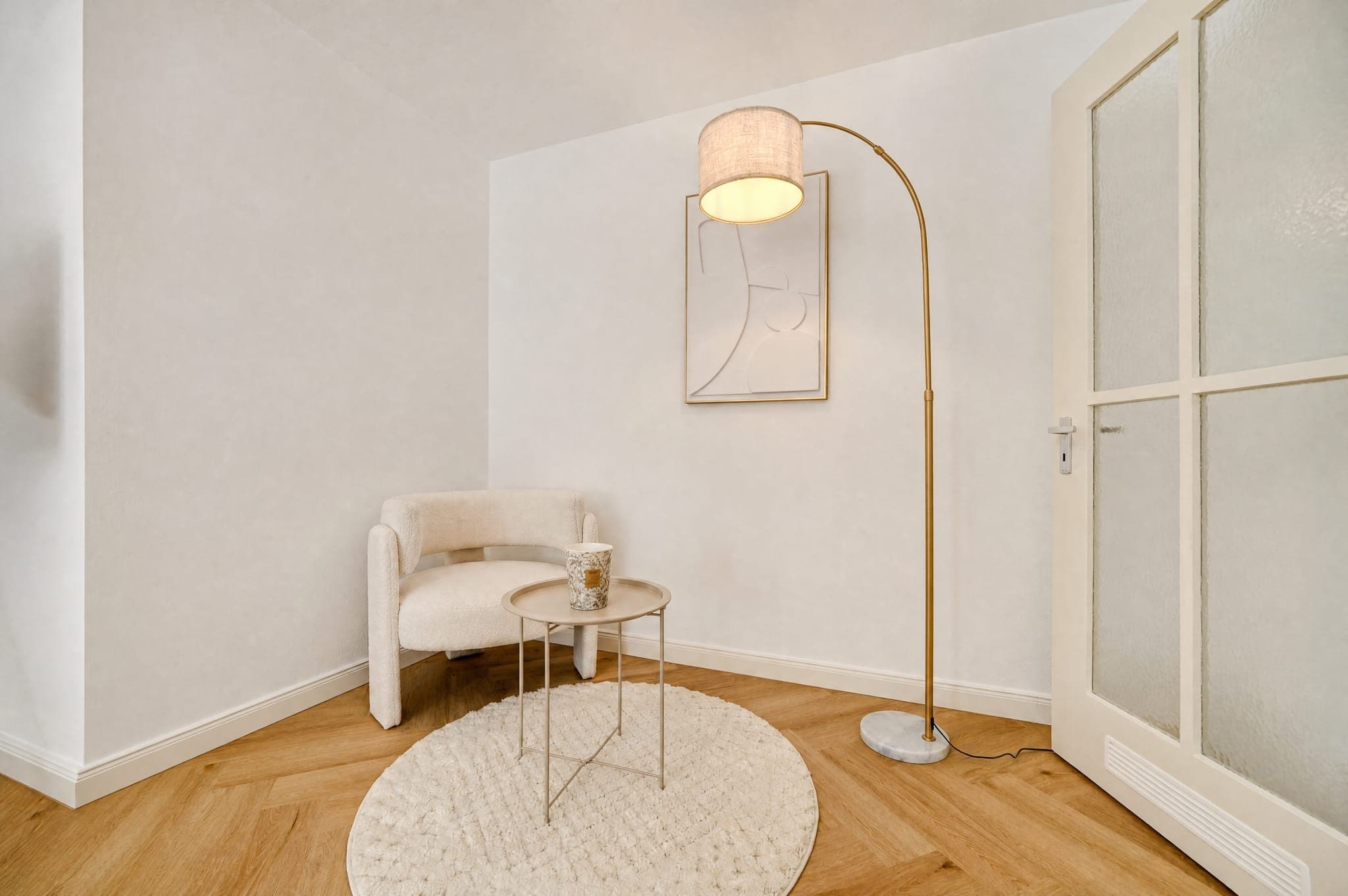 Sitting area with an upholstered armchair, side table and arc lamp against a pale wall