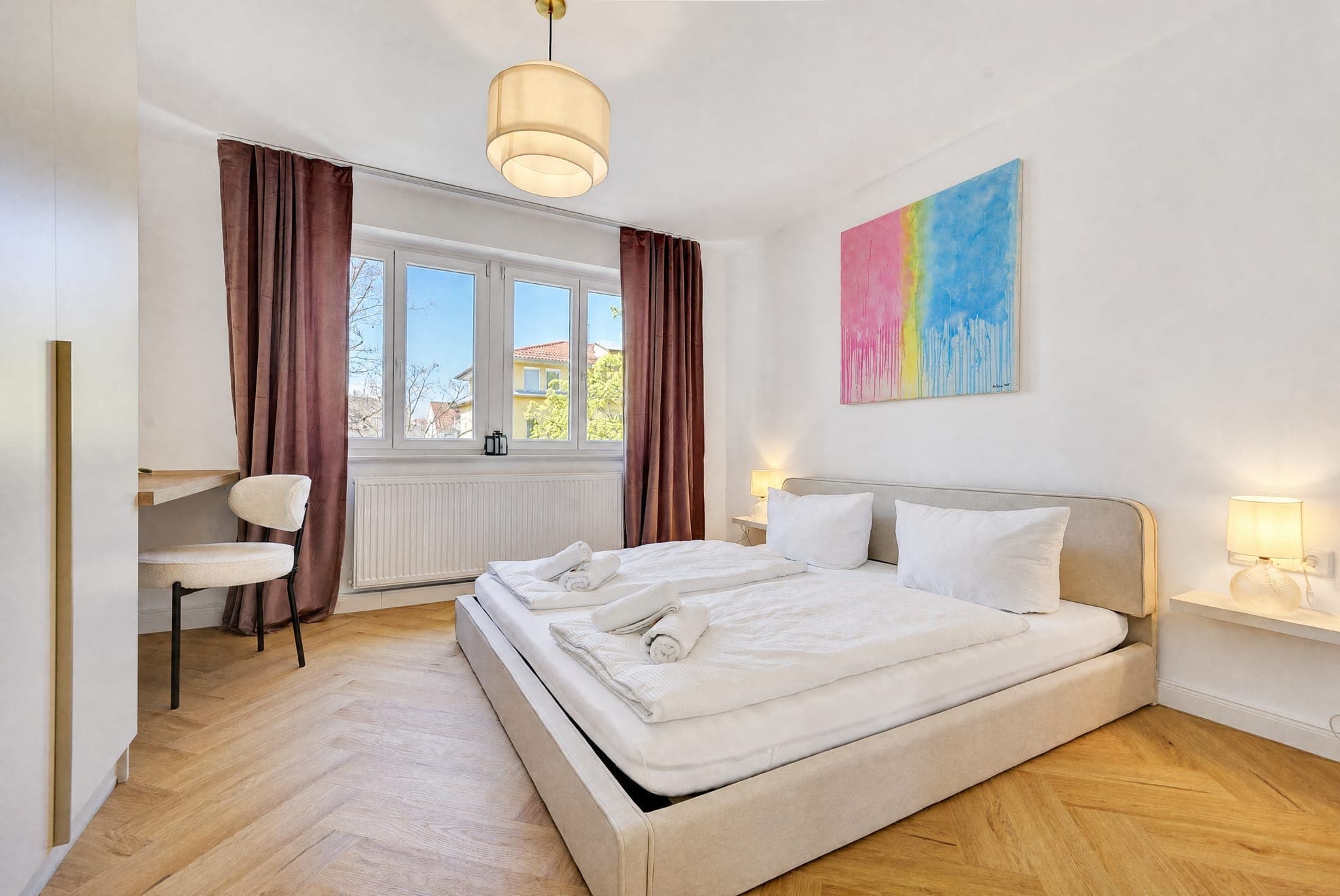 Bedroom with a double bed, burgundy curtains and a view over the neighbouring roofs