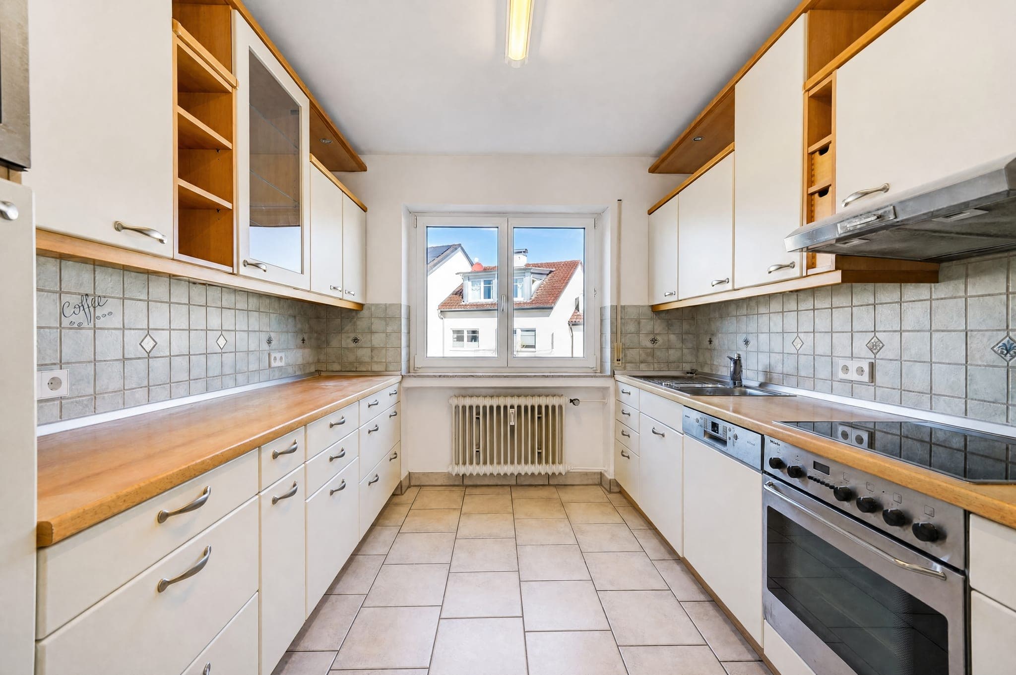 Narrow galley kitchen with a wooden worktop, wall units and a window between the runs