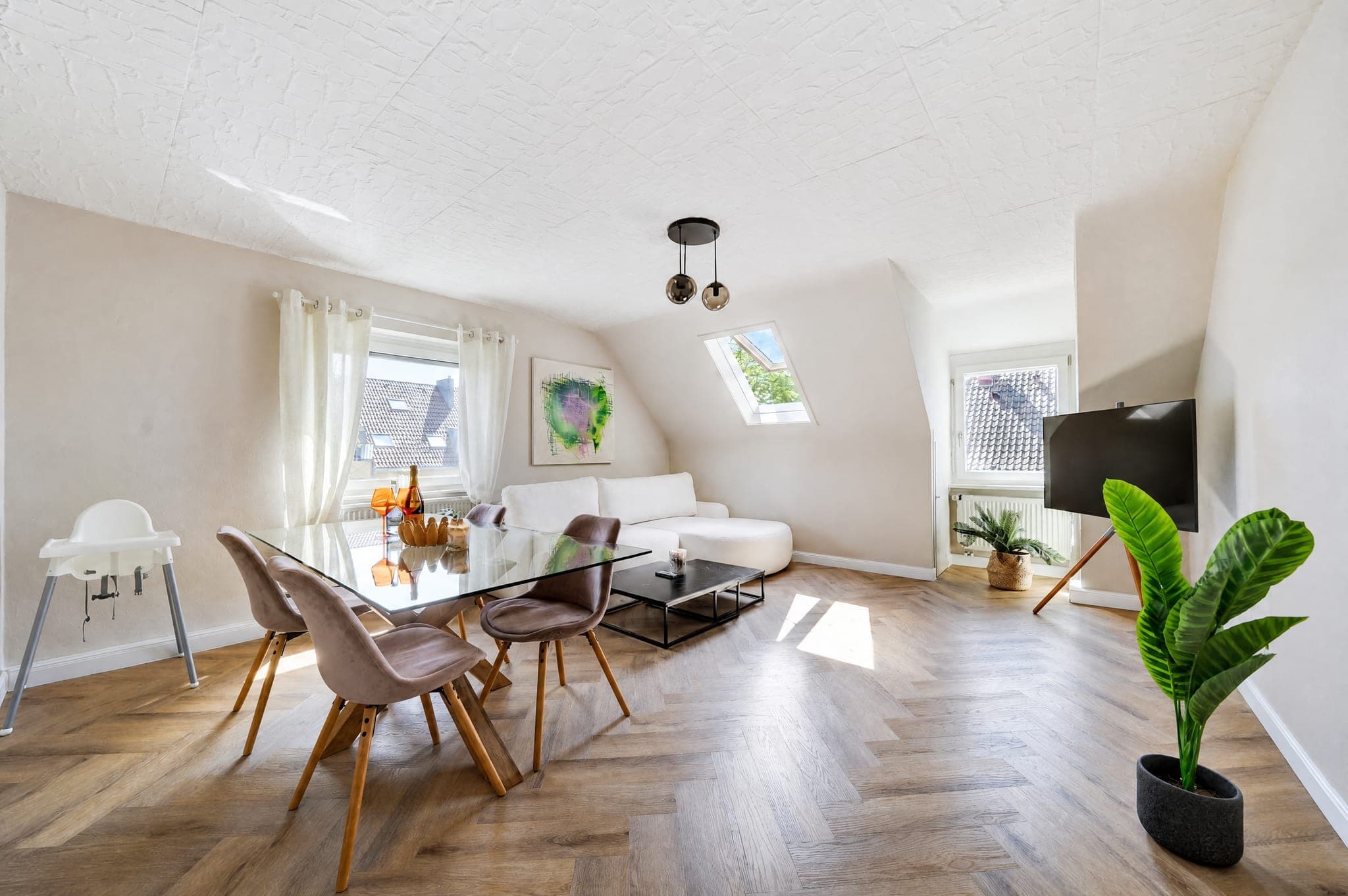 Dining area with a glass table and high chair beside the sofa under the sloped ceiling