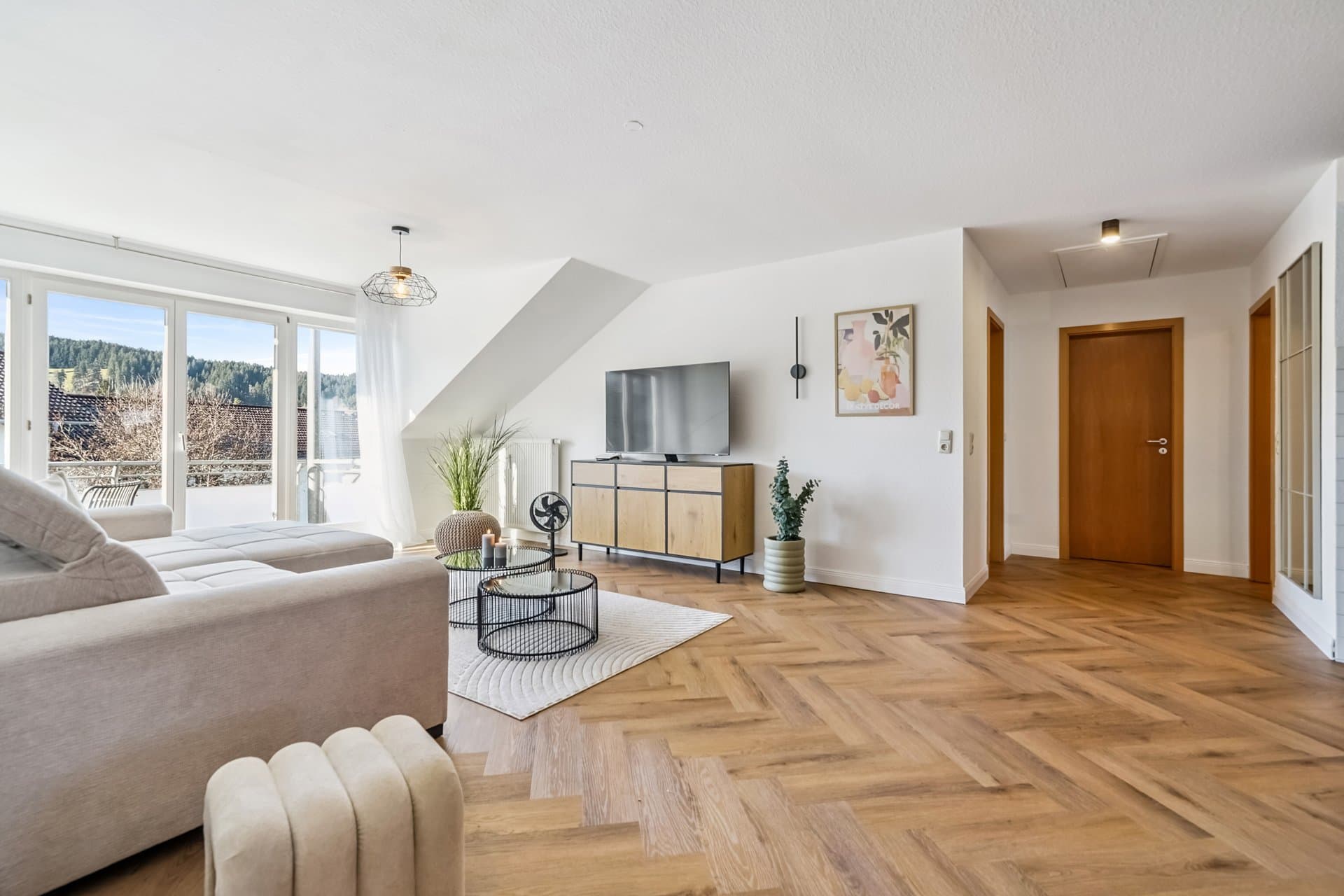Attic living room with a pale sofa, TV sideboard and a window front onto greenery