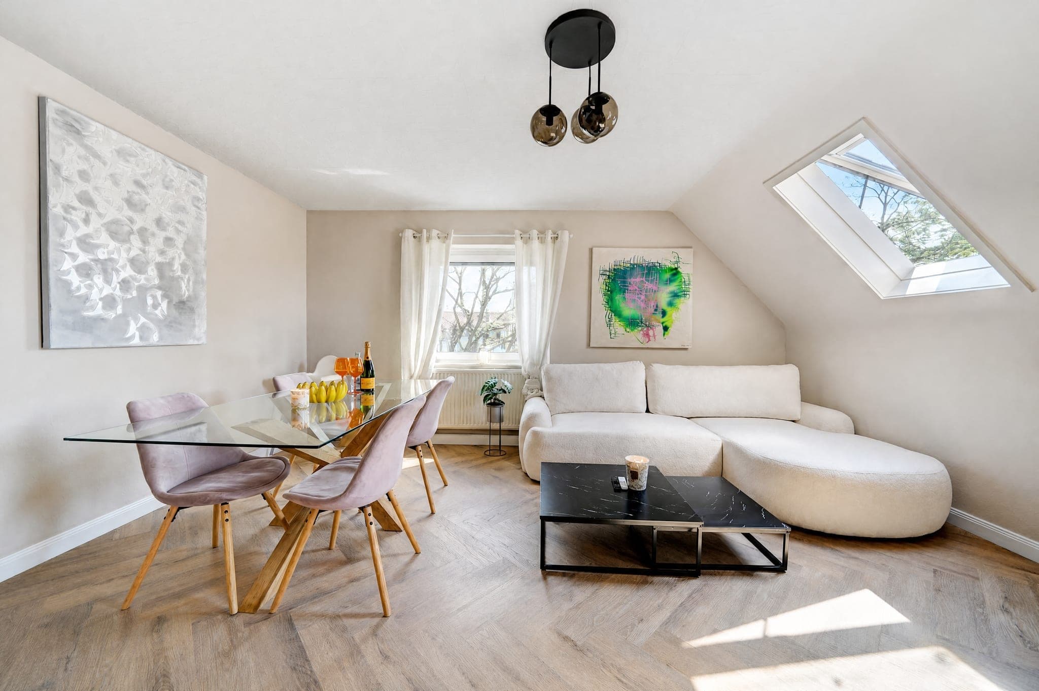 Dining spot with a glass table and rosé chairs under the sloped ceiling, beside a rounded sofa