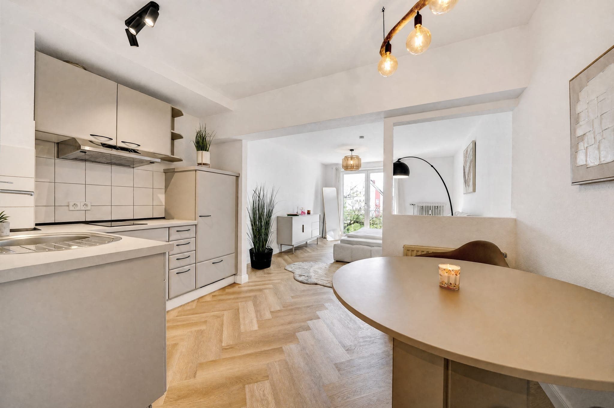 Open-plan kitchen with a pale run of units and an oval dining table on herringbone parquet