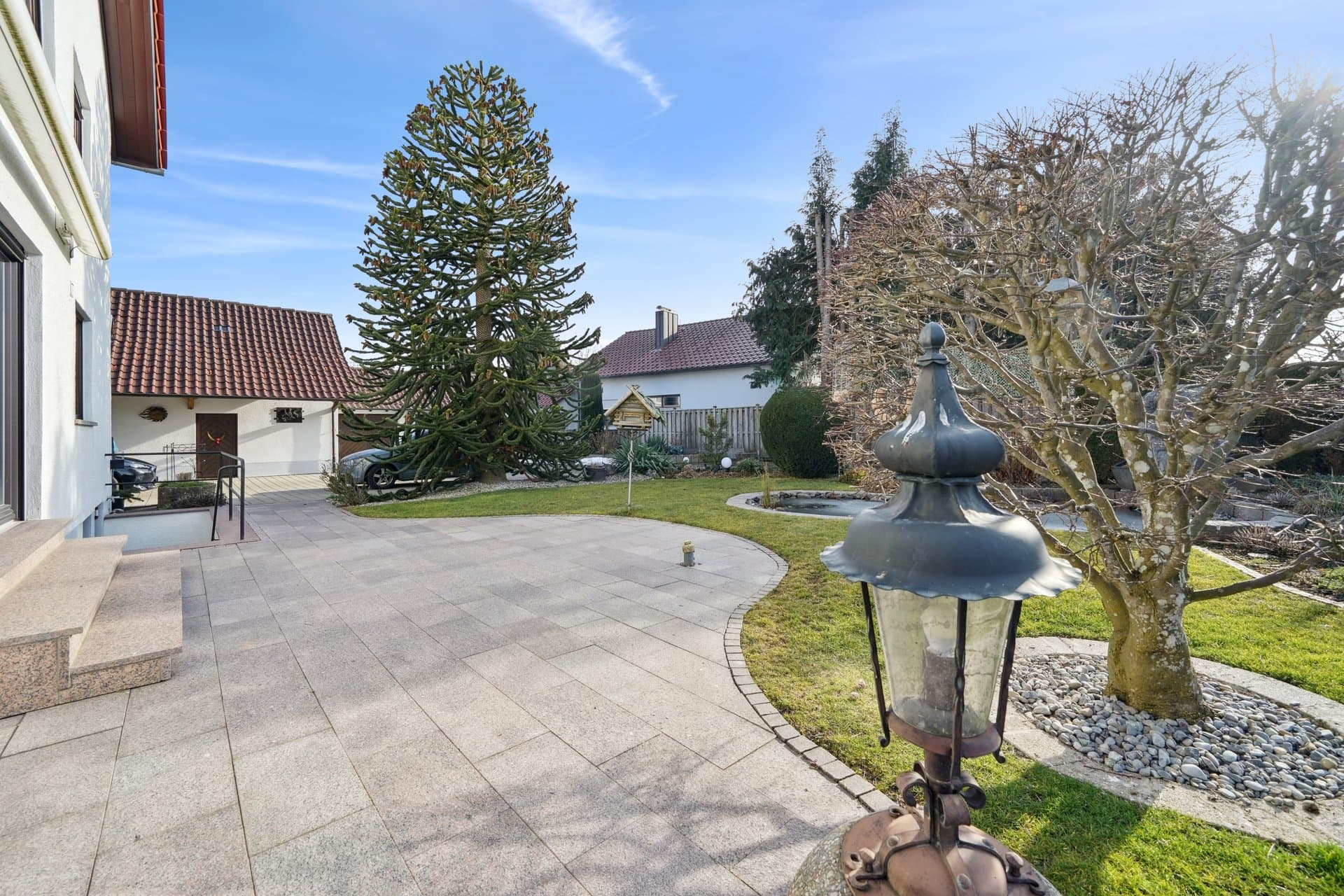 Paved driveway with a garden lantern in front of the house, tiled roof against a blue sky